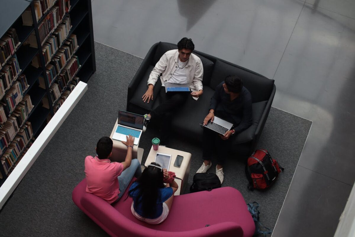 A group of diverse adults collaborating on laptops in a library's lounge area.