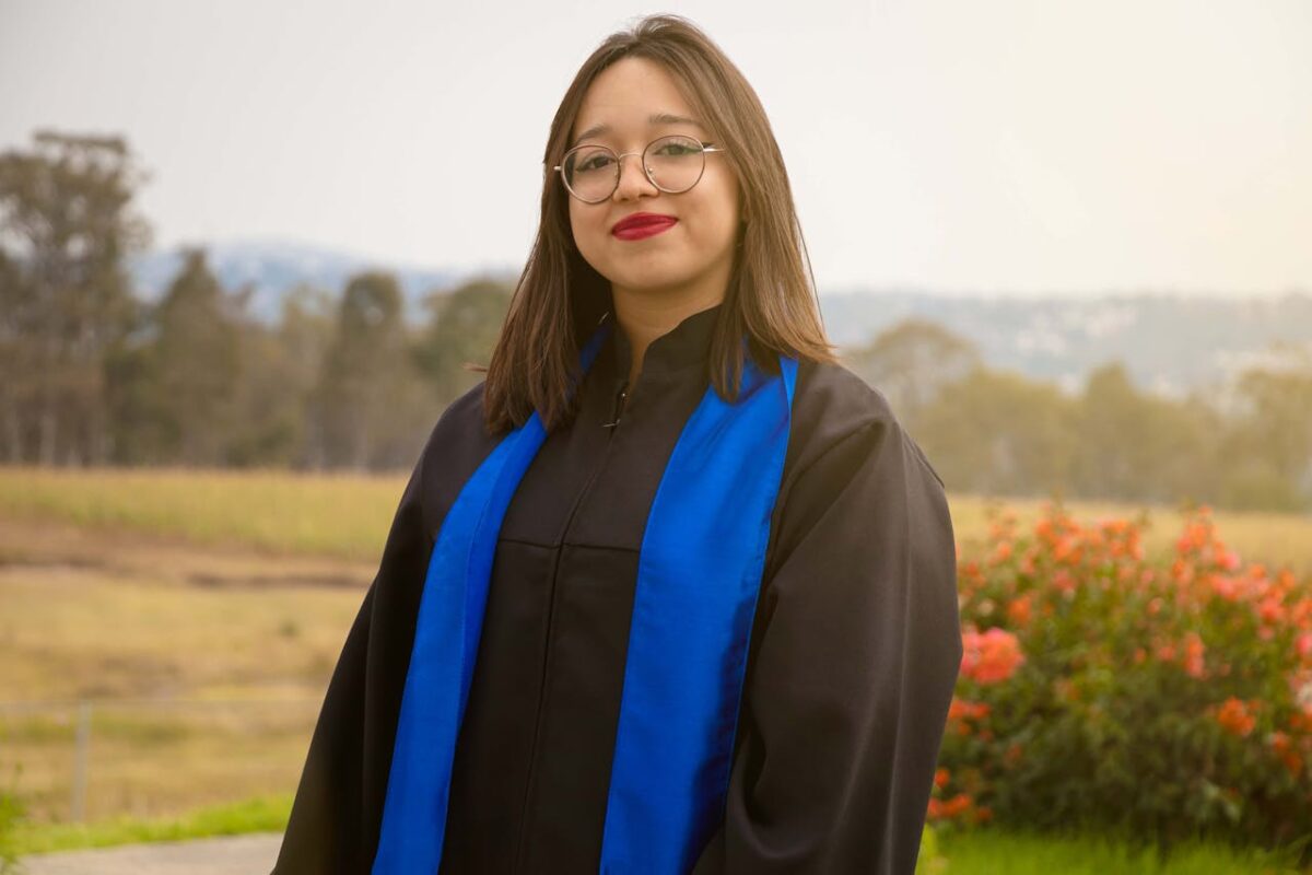 A university graduate wearing a gown celebrates her achievement outdoors in México.