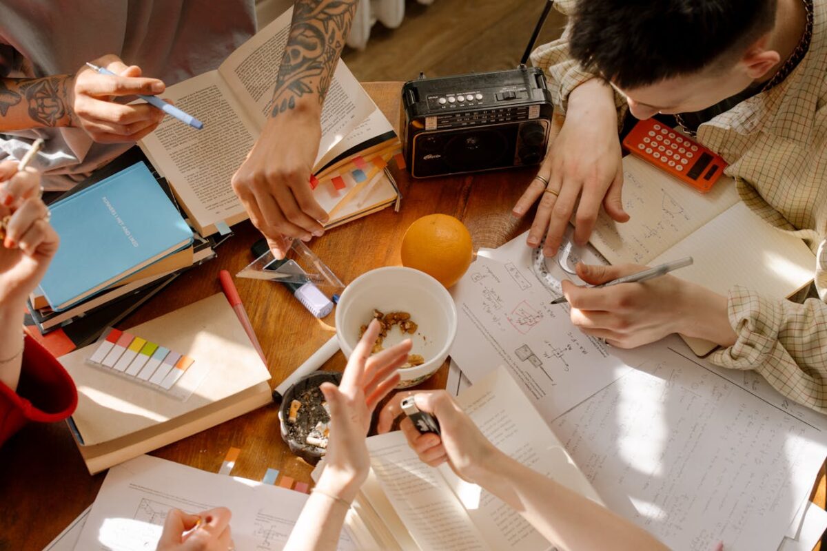 Students engaging in a collaborative study session with books and notes on a wooden table.